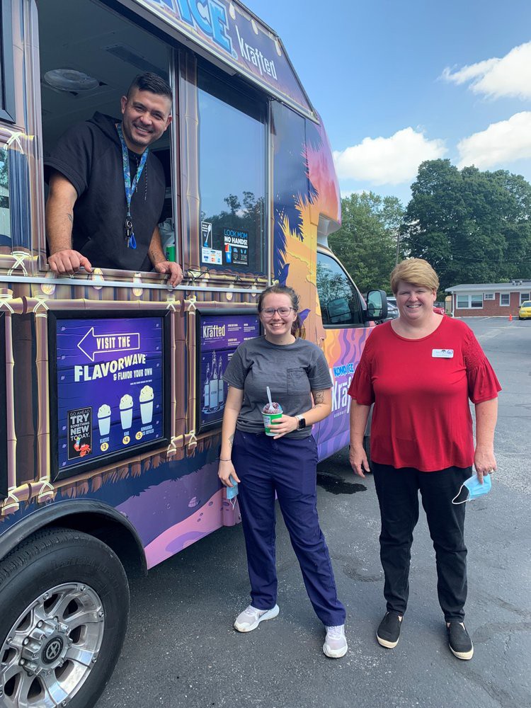 Three people, two standing outside and one leaning out of a colorful food truck.