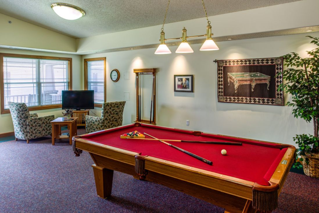 A cozy game room with a red-felt pool table and comfortable seating area.