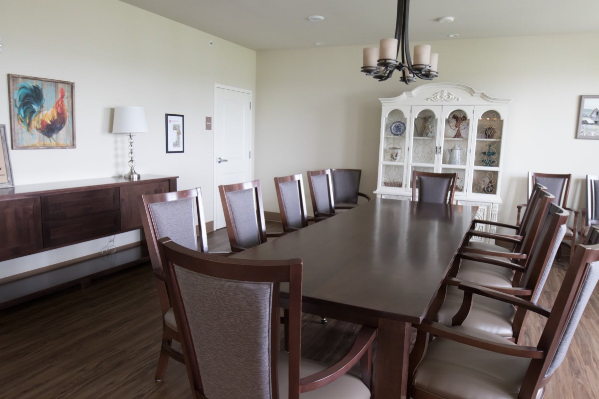 A spacious dining room with a long table, multiple chairs, and a decorative cabinet.