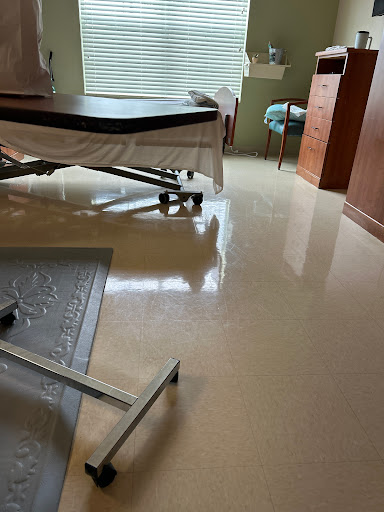A view of a hospital room featuring a bed, furniture, and polished flooring.