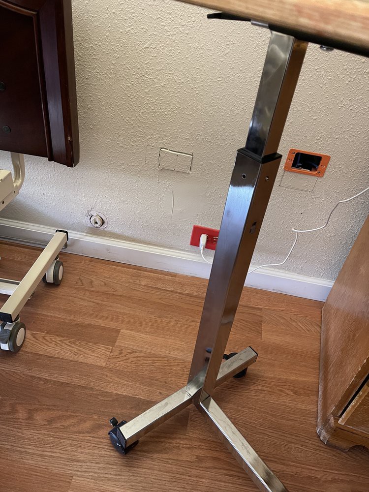 A metal stand with wheels sits on a hardwood floor next to a wall outlet.
