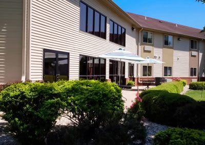 A sunny day outside a building with a patio and well-maintained garden.