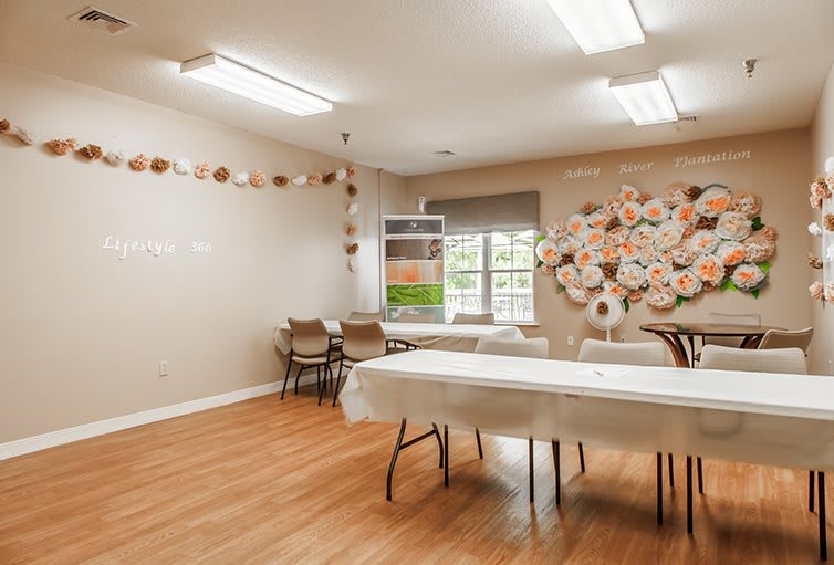A well-lit classroom with decorated walls, tables, and chairs arranged on a hardwood floor.