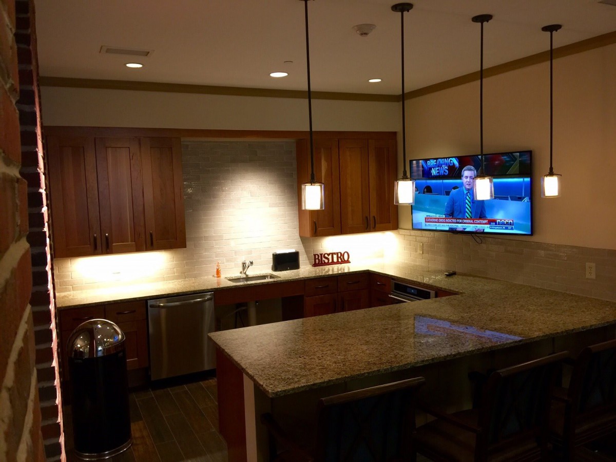 A modern kitchen with wooden cabinets, an island, pendant lighting, and a wall-mounted TV.