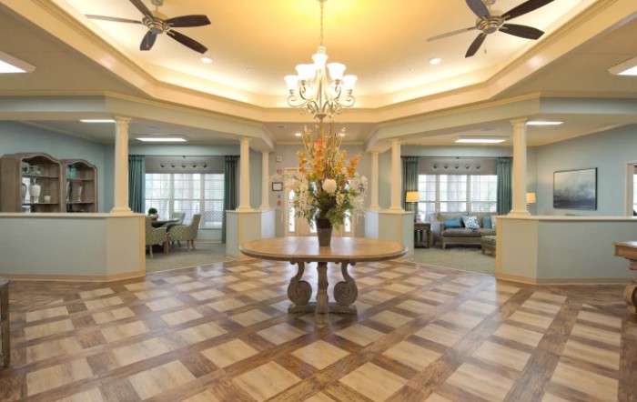 An elegant living room with a decorative wooden floor, featuring a central table adorned with flowers under a chandelier.