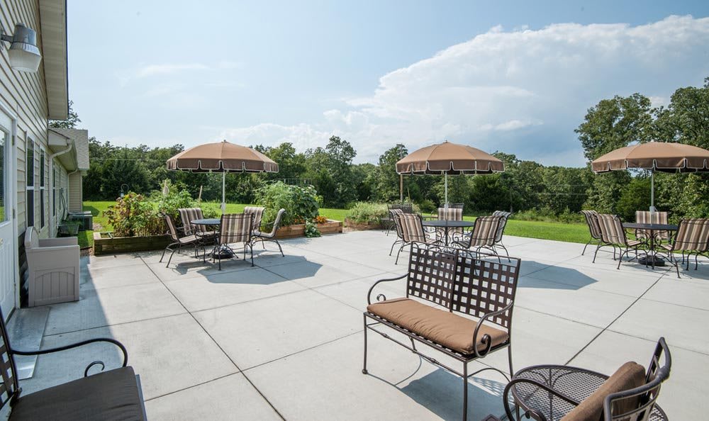 A sunny outdoor patio with tables, chairs, and umbrellas overlooking a lush landscape.