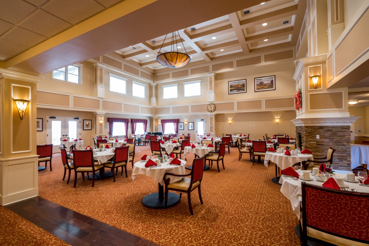An elegant restaurant dining area with neatly arranged tables and chairs, featuring a stylish ceiling design and chandelier.