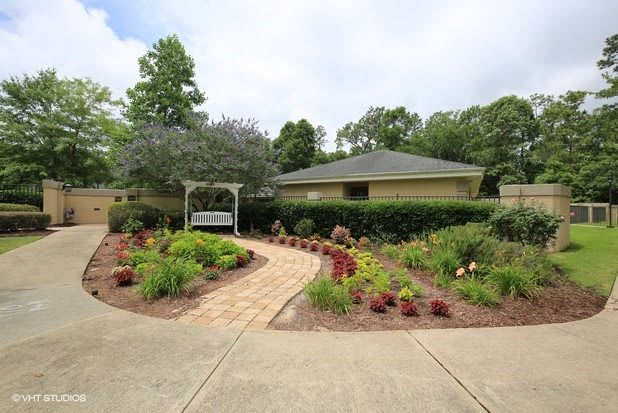 A beautifully landscaped garden with a winding pathway leading to a small building, surrounded by lush greenery and colorful plants.