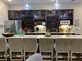 A modern kitchen with pendant lights, bar stools, and integrated wine racks.