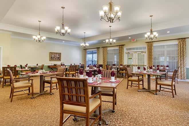 An elegant dining room setup with neatly arranged tables and chairs, adorned with chandeliers and a warm ambiance.