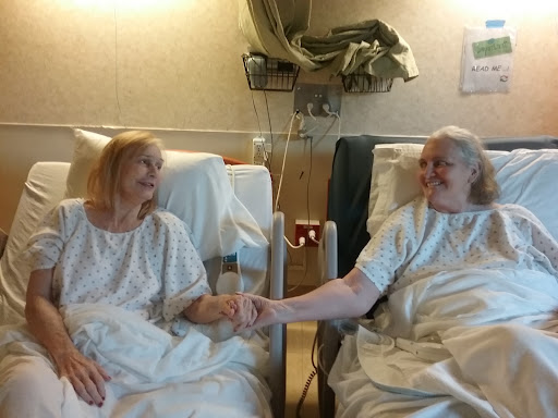 Two patients in a hospital bed share a moment of connection and support.