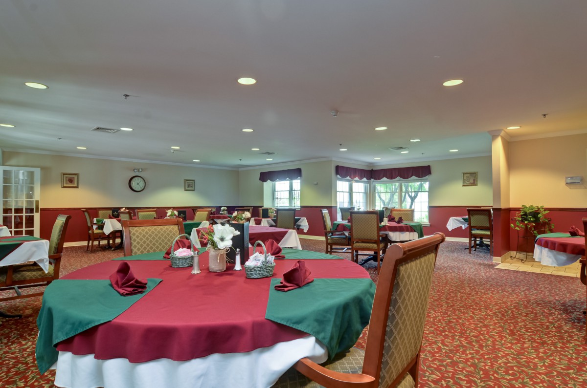 A spacious dining room with tables set for a meal, featuring red and green tablecloths.