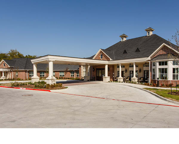 A large building with a covered entrance and columns, surrounded by landscaped grounds.