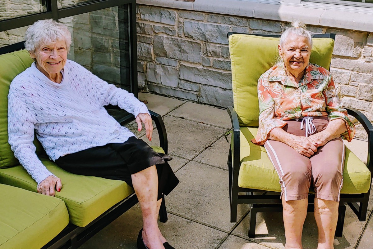 Two elderly women sitting and relaxing on outdoor patio chairs.