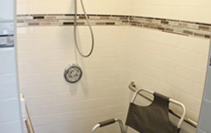 An accessible bathroom with a shower chair and handheld showerhead.