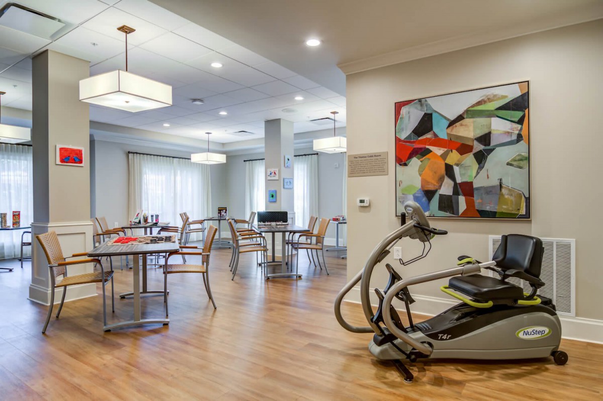 A modern indoor space featuring exercise equipment and a dining area with contemporary artwork on the wall.