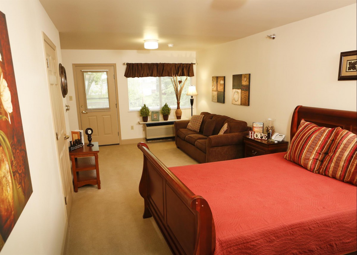 A cozy bedroom with a large bed and a sofa, featuring warm decor and natural light.