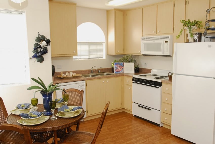 A cozy kitchen with light wooden cabinets, complete with a stove, microwave, and refrigerator. A small dining table is set for two.