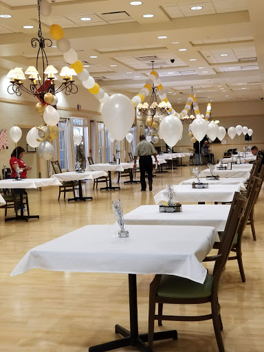 A spacious dining hall set up for an event, featuring neatly arranged tables adorned with white tablecloths and decorative balloons.