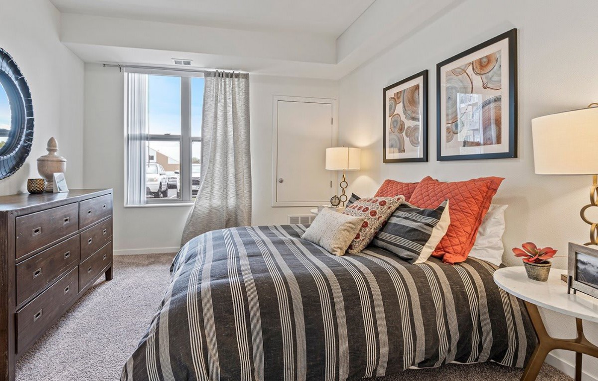 A modern bedroom with a striped bedspread, two framed artworks above the bed, and a window with curtains.