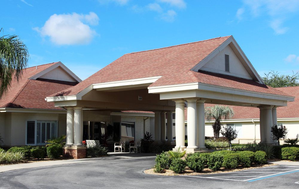 A building with a covered entrance supported by columns and surrounded by landscaping.