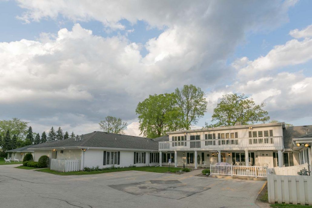 A large two-story building with a cloudy sky in the background and trees surrounding the area.