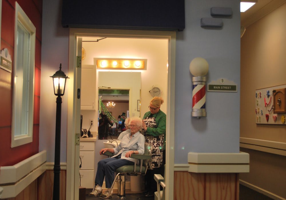 A cozy barbershop with a person receiving a haircut while sitting in a chair, under the warm glow of lights.