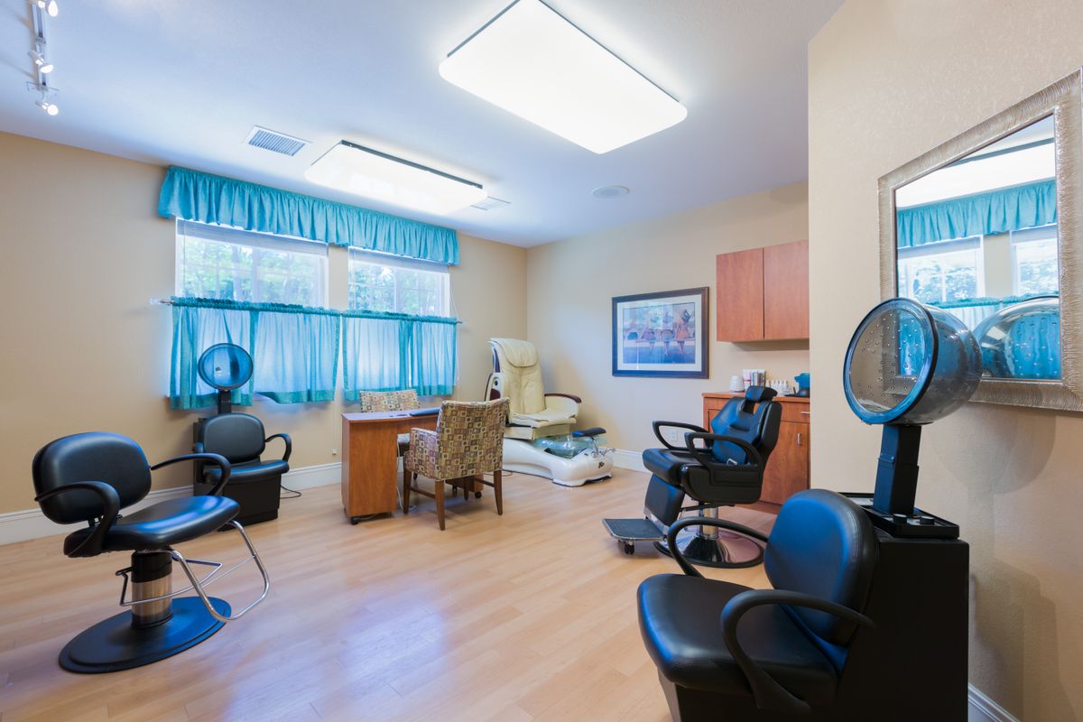 The image shows the interior of a hair salon with styling and dryer chairs, a wooden floor, and large windows.