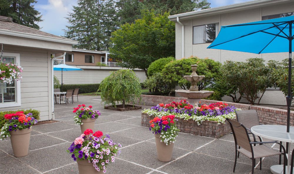 A beautifully landscaped outdoor patio featuring colorful potted flowers and a central fountain.