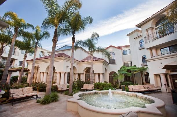 A beautiful courtyard with a central fountain surrounded by palm trees and Mediterranean-style architecture.