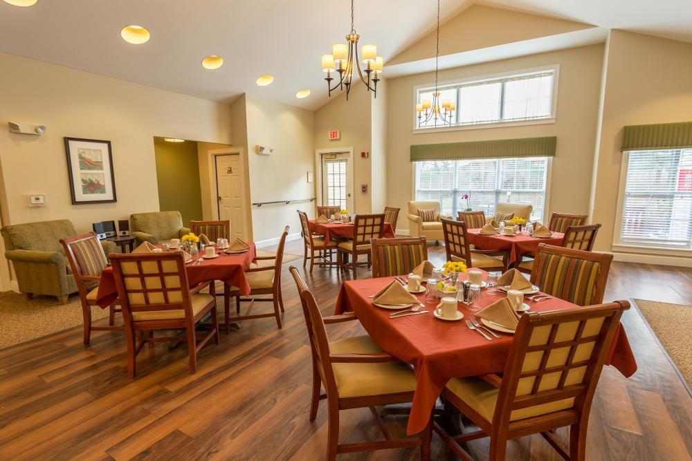 A cozy dining room with neatly set tables and chairs, featuring a warm ambiance and large windows.