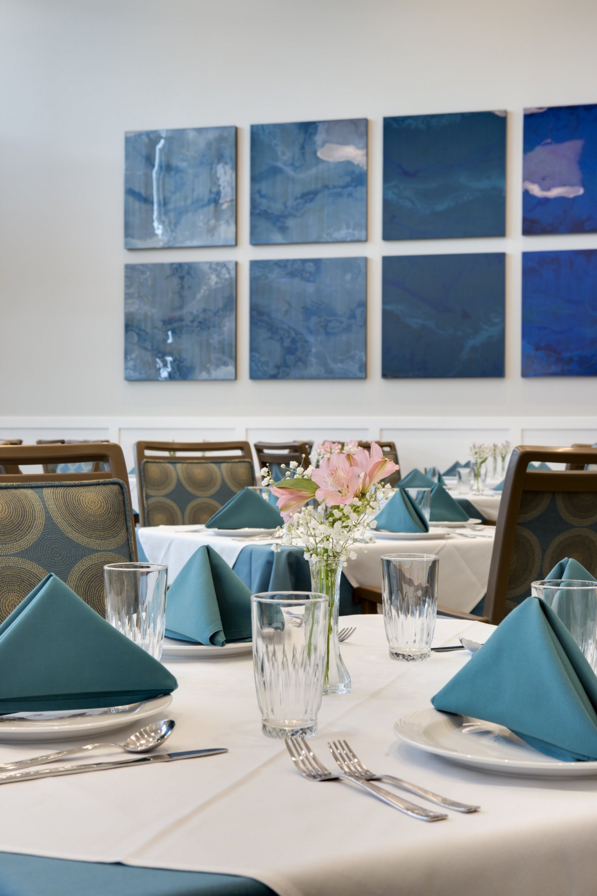 A beautifully set dining table in a restaurant featuring elegant teal napkins and modern artwork on the wall.