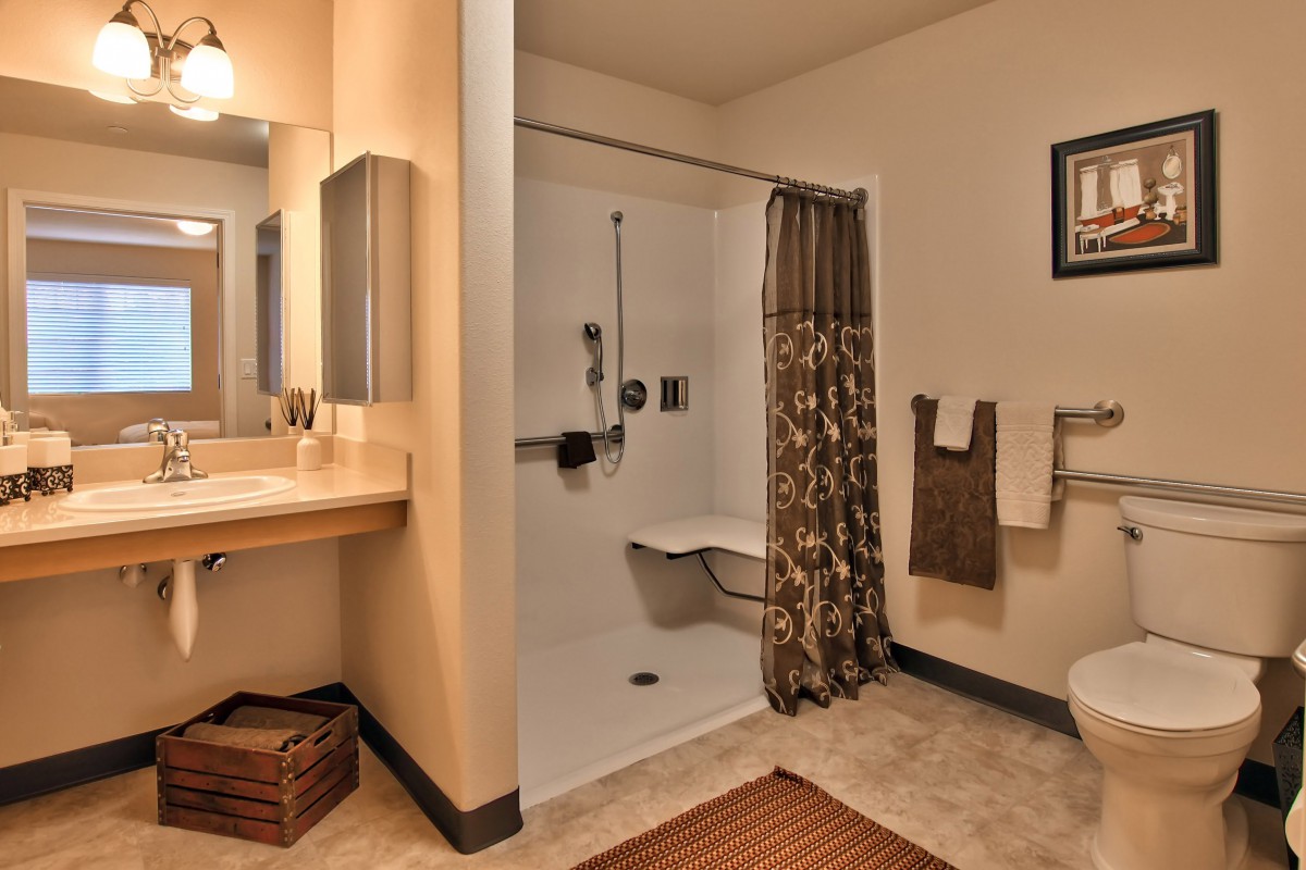 An accessible bathroom featuring a shower with a seat, sink, and towel rack.