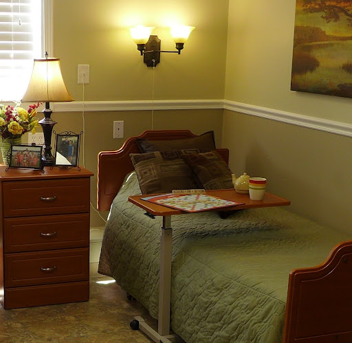 A cozy hospital room featuring a neatly made bed, a bedside lamp, and a small nightstand with flowers.