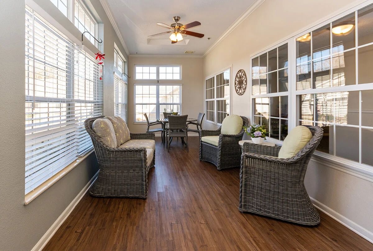 A bright sunroom with wicker furniture and large windows, featuring a ceiling fan and hardwood floors.