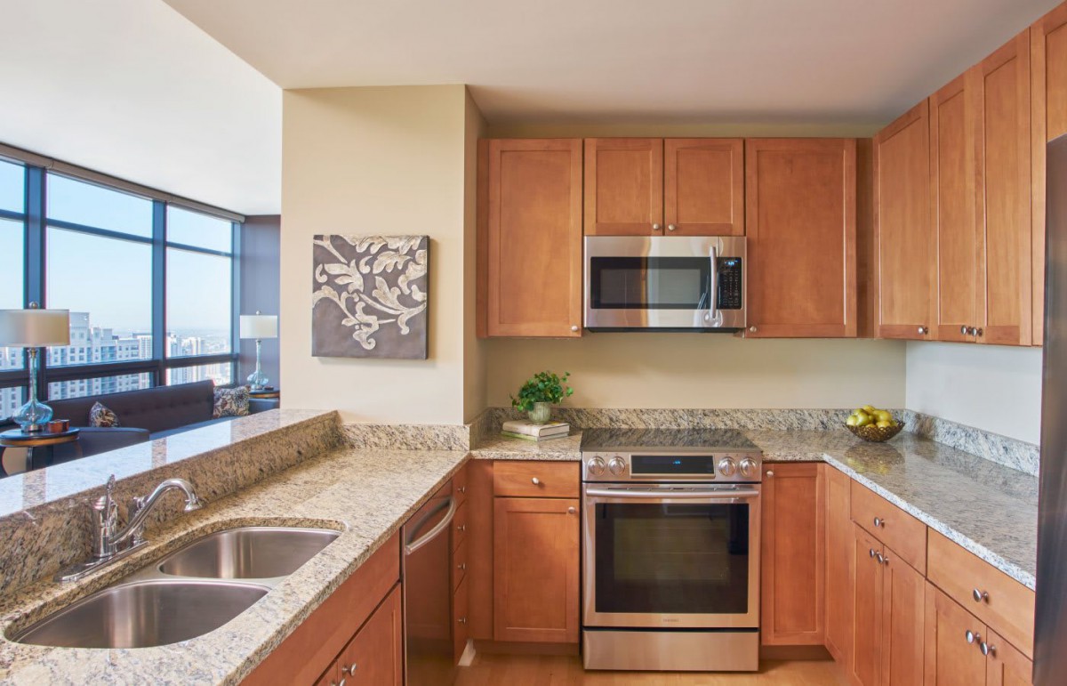 A modern kitchen with wooden cabinets and granite countertops, featuring a microwave and oven.