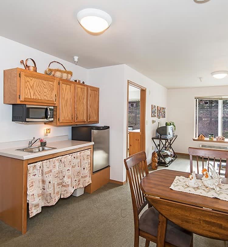 A cozy kitchen and dining area featuring wooden cabinets, a dining table with chairs, and a microwave.