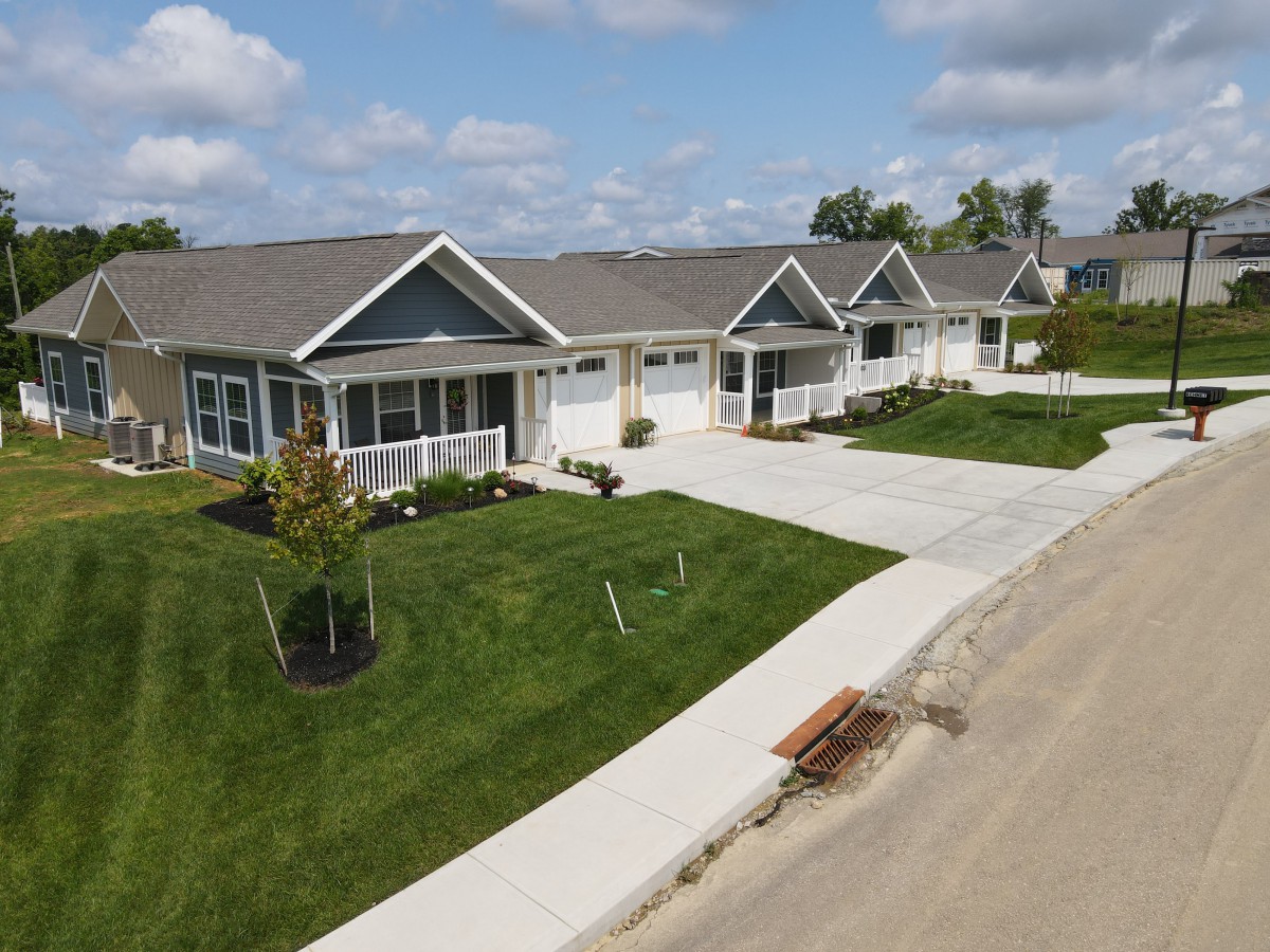 A row of suburban houses with well-maintained lawns and driveways, set under a partly cloudy sky.