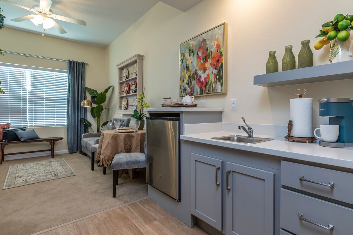 A modern kitchen area with elegant decor, featuring a small sink, stainless steel appliances, and colorful artwork.