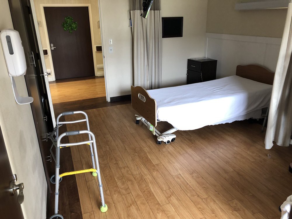 An empty hospital room with a bed and a walker beside it.