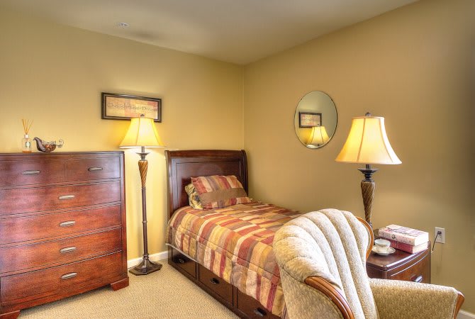 A cozy bedroom featuring a single bed with striped bedding, wooden furniture, and warm lighting from lamps.