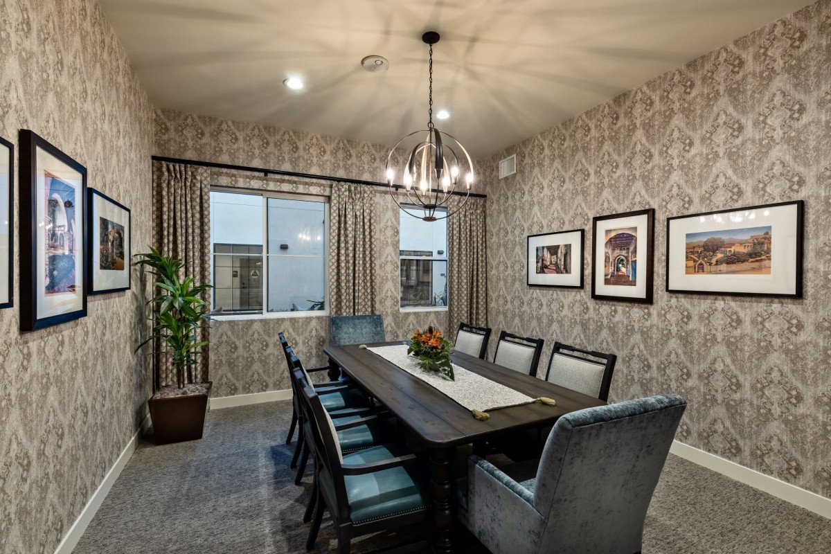 A stylish dining room featuring a large table with upholstered chairs, elegant wallpaper, and a modern chandelier.