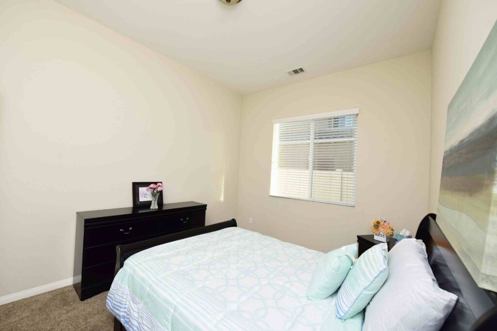 A simple bedroom with a bed and dresser, featuring a window providing natural light.