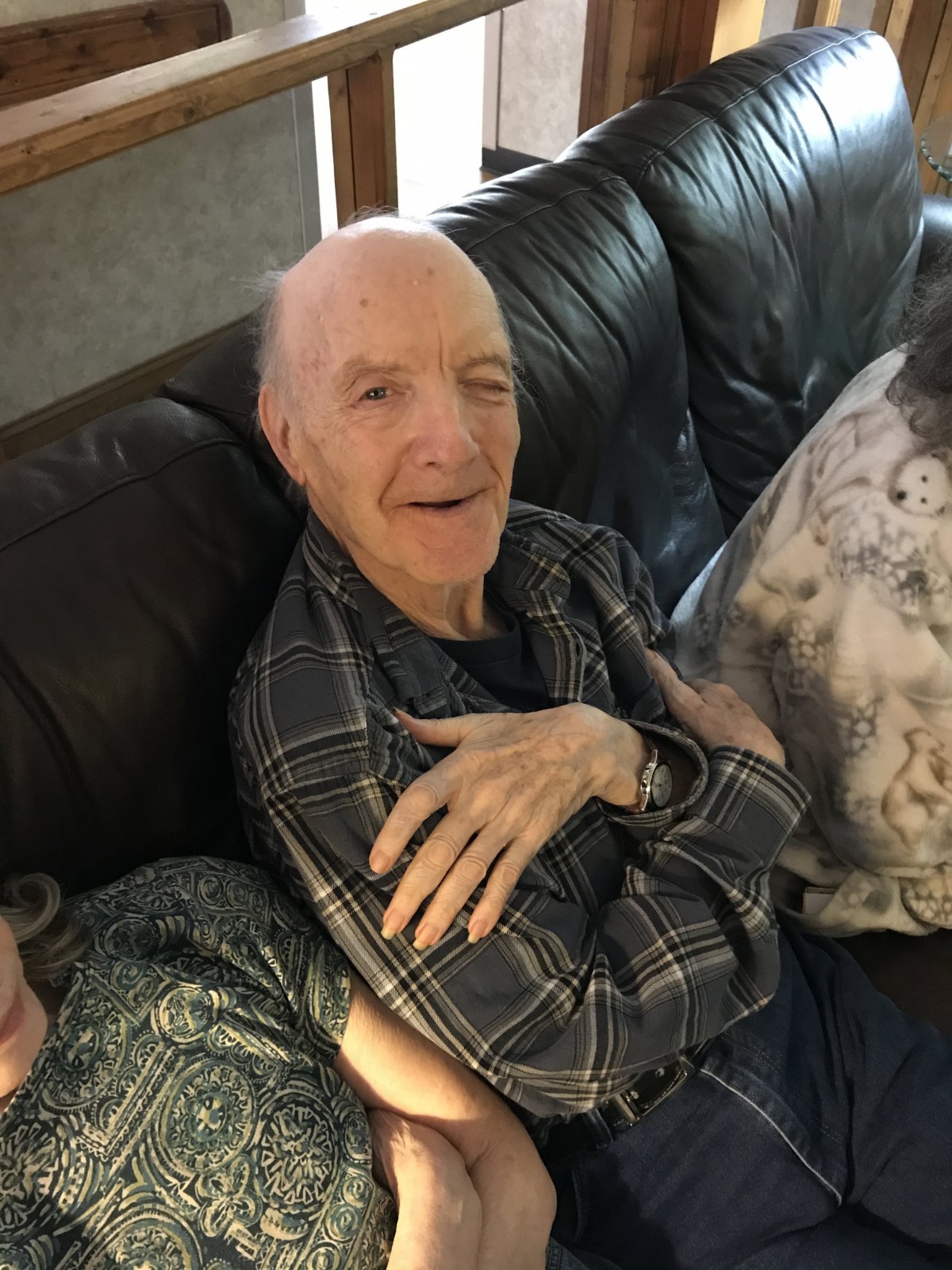 An elderly man smiling while sitting on a couch indoors.