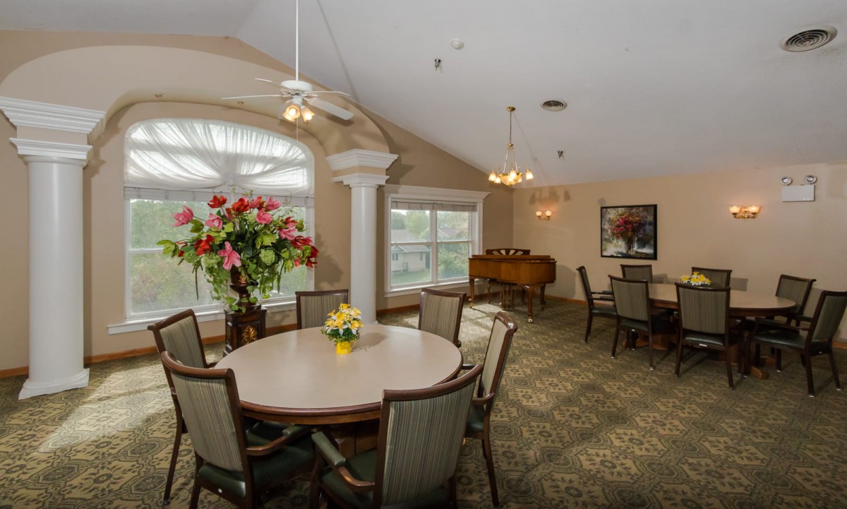 A well-lit dining area with tables and chairs, decorated with vibrant flowers.