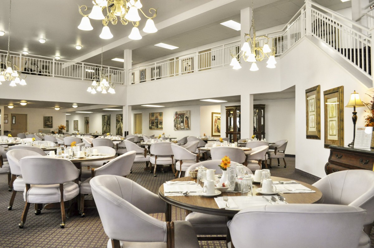 An elegant dining area featuring well-set tables and comfortable chairs under ornate chandeliers.