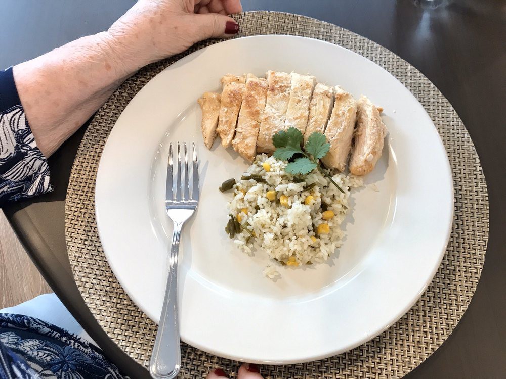 A neatly plated meal of sliced chicken breast and risotto garnished with herbs.