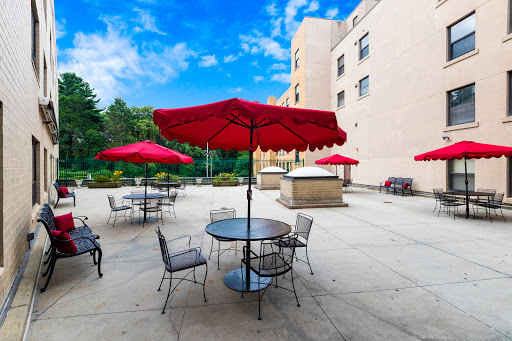 A relaxing outdoor patio area with red umbrellas providing shade over tables and chairs, set against a bright blue sky.