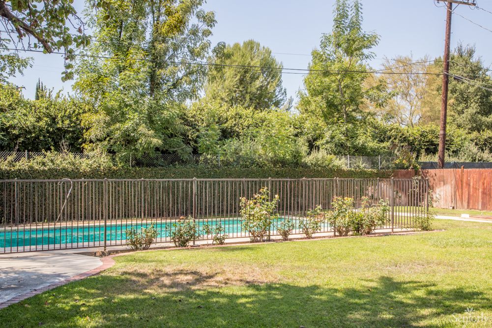 A fenced swimming pool surrounded by a garden with trees.
