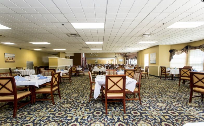 An empty restaurant dining area with neatly arranged tables and chairs on a carpeted floor.
